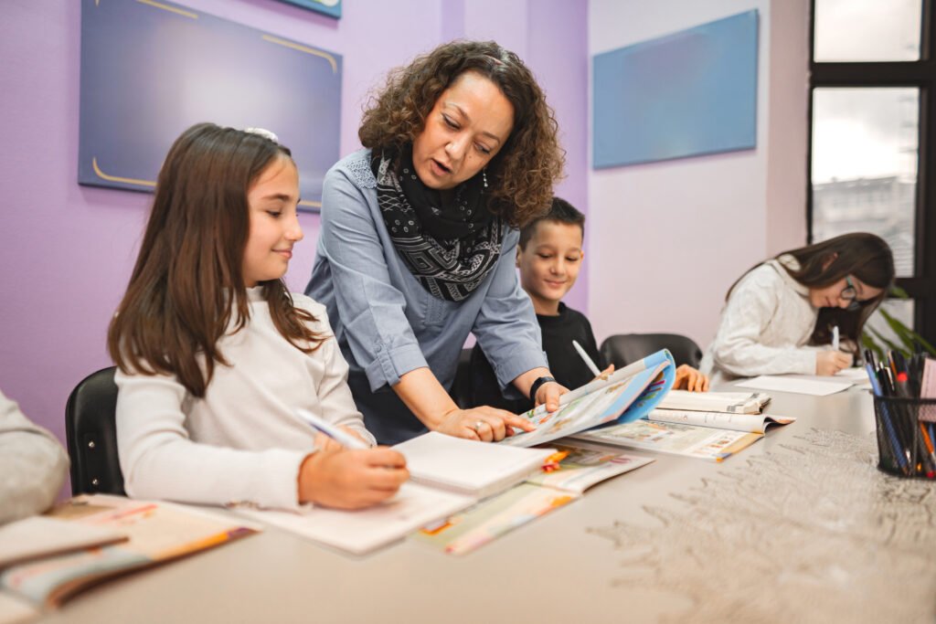 Female teacher helping elementary students at language school class.